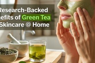 A cup of matcha green tea surrounded by fresh tea leaves and a bottle of green tea face serum.