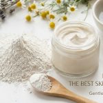 A bowl of pure white Kaolin clay powder next to a natural face mask applicator brush and fresh green leaves.