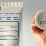 A person checking the expiration date on the back of a yellow sunscreen tube.
