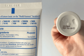 A person checking the expiration date on the back of a yellow sunscreen tube.